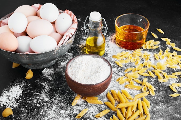 Pâtes isolées sur une surface recouverte de farine avec des ingrédients de côté.