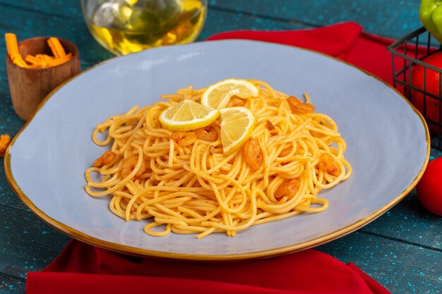 Pâtes italiennes cuites avec des tranches de citron à l'intérieur de la plaque bleue avec de l'huile et des légumes sur bleu