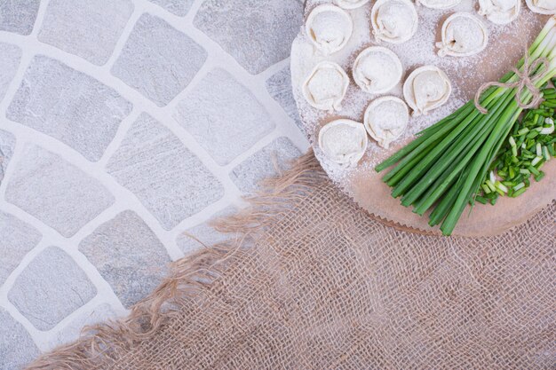 Pâtes de khinkali crues sur la farine avec un bouquet d'oignon vert.