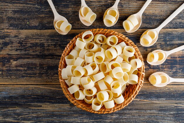 Pâtes macaroni dans un bol et des cuillères sur un fond en bois foncé. vue de dessus.