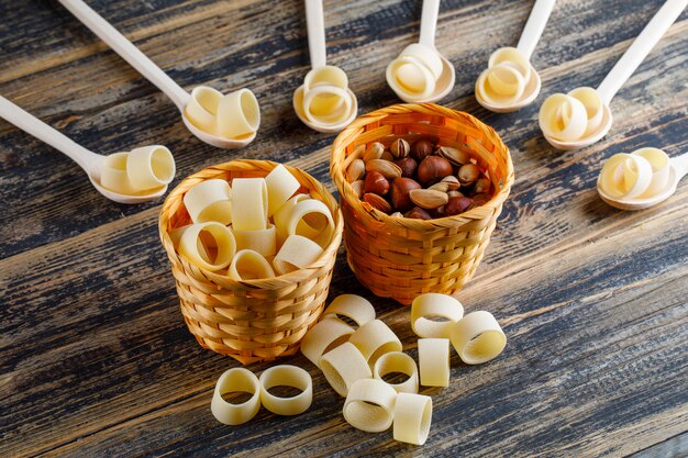 Pâtes macaroni dans des bols et des cuillères avec pistache et noisette high angle view sur un fond en bois foncé