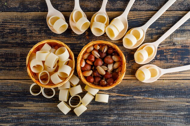 Pâtes macaroni dans des bols et des cuillères avec pistache et noisette vue de dessus sur un fond en bois foncé