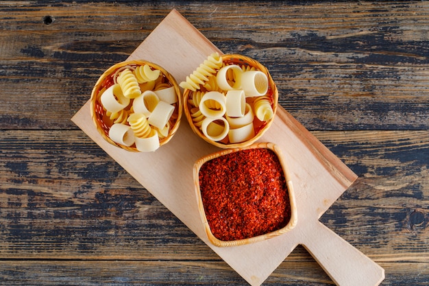 Pâtes macaroni dans des seaux avec vue de dessus d'épices rouges sur une planche à découper et fond en bois