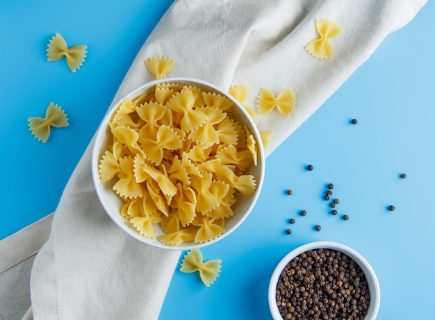 Photo gratuite pâtes macaroni à plat dans un bol avec du poivre noir dans un petit bol sur un chiffon