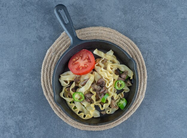 Pâtes avec des morceaux de boeuf sur une poêle noire.