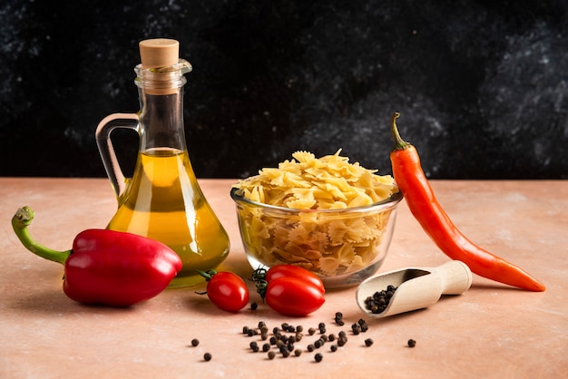 Pâtes non cuites, légumes et bouteille d'huile sur table orange.