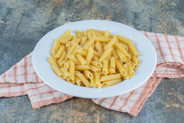 Pâtes penne sur l'assiette, sur la serviette, sur le fond marbré.