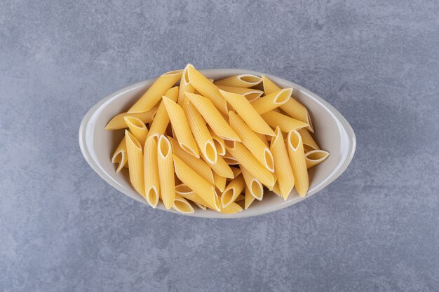 Pâtes penne crues dans un bol en céramique.