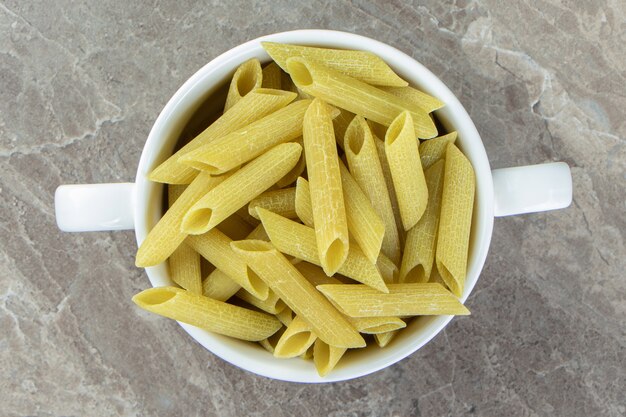 Pâtes penne crues dans une tasse blanche.