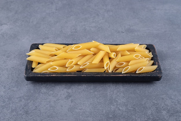 Pâtes penne crues sur plaque noire.