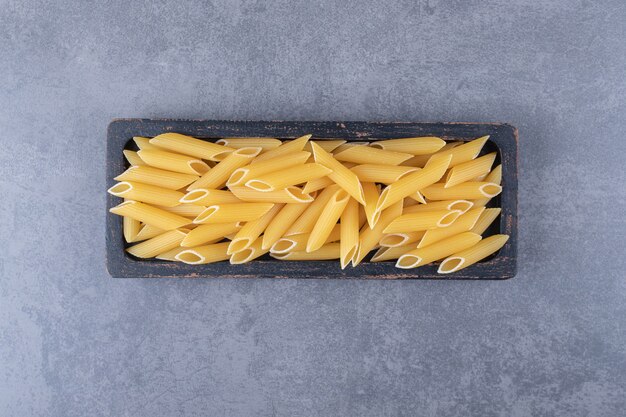 Pâtes penne crues sur plaque noire.