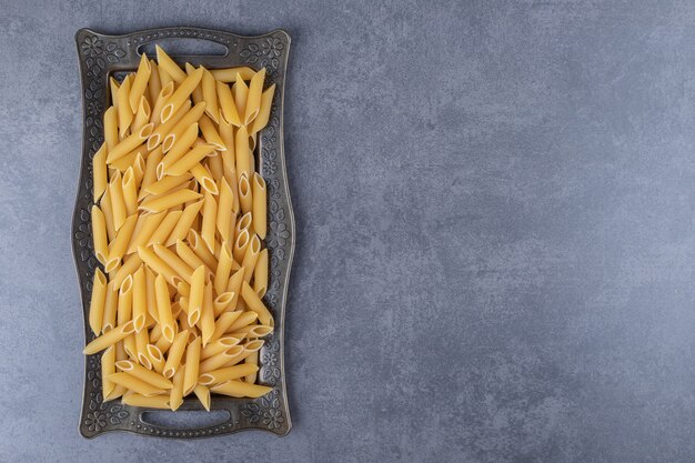 Pâtes penne crues sur plateau sombre.