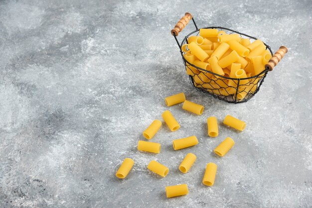 Pâtes Penne dans un récipient métallique sur une table en marbre gris.