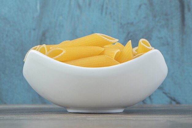 Pâtes penne non cuites dans un bol blanc.