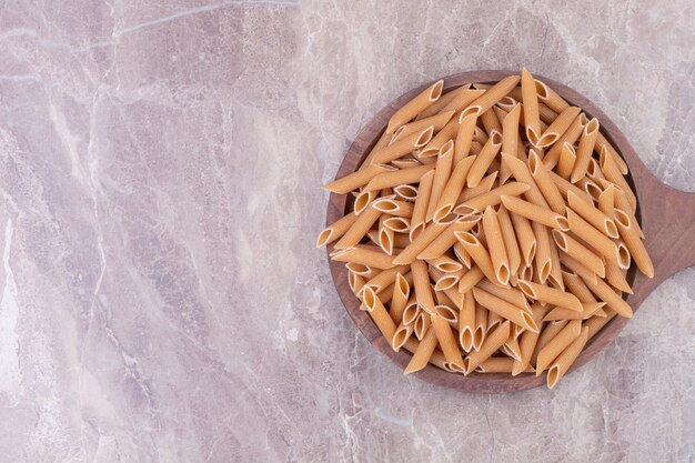 Pâtes penne sur un plateau en bois sur le marbre