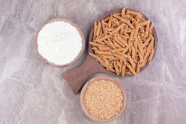 Pâtes sur un plateau en bois avec du blé et de la farine mélangée dans des tasses