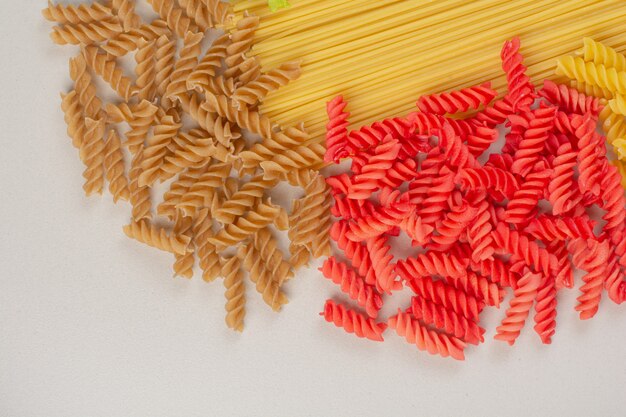 Pâtes et spaghettis en spirale non cuits colorés sur une surface blanche