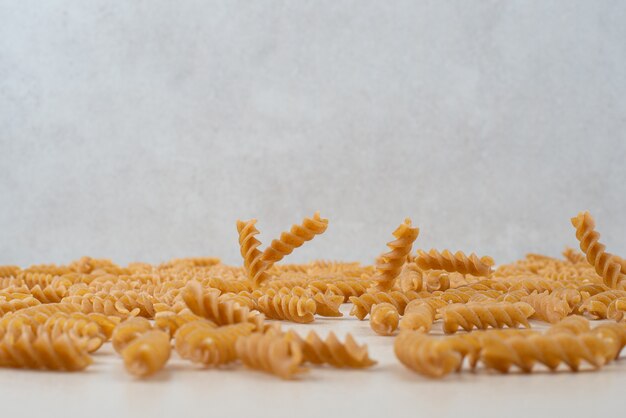 Pâtes en spirale crues dispersées sur une surface blanche.