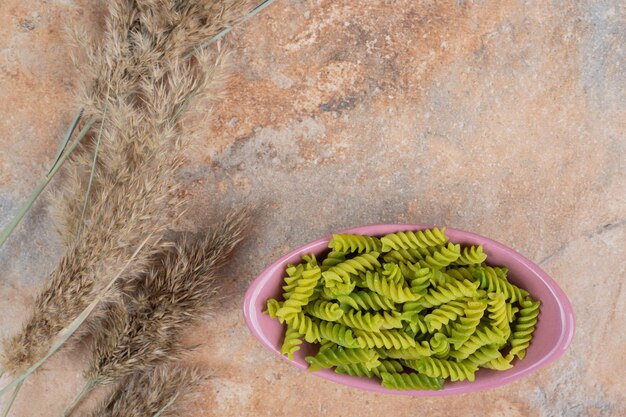 Pâtes en spirale verte non préparées sur bol rose.