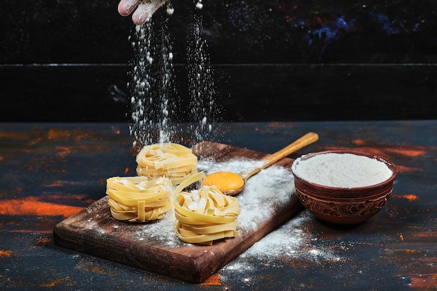 Photo gratuite pâtes tagliatelles crues sur planche de bois avec bol de poudre.