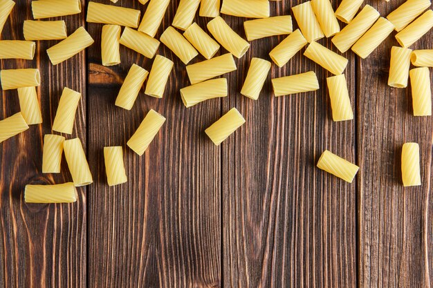 Pâtes tortiglioni épars sur table en bois, mise à plat.