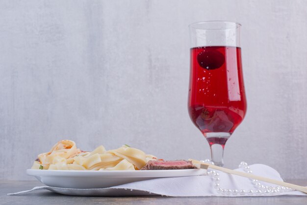 Pâtes à la viande et verre de limonade rouge sur plaque blanche