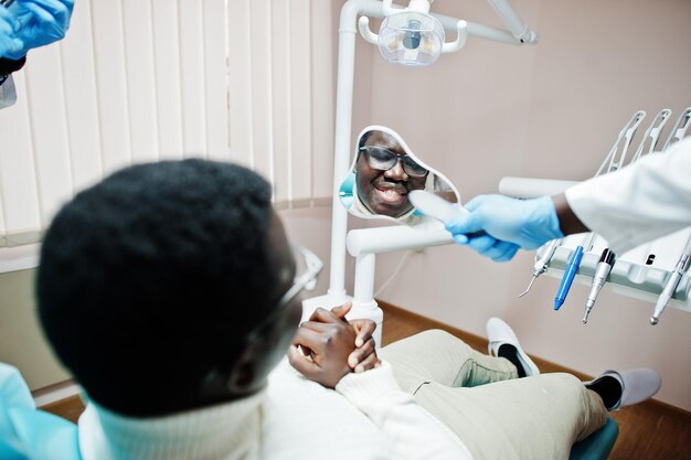 Patient afro-américain dans un fauteuil dentaire Cabinet de dentiste et concept de cabinet médical Dentiste professionnel aidant son patient à la médecine dentaire et lui montrant un miroir