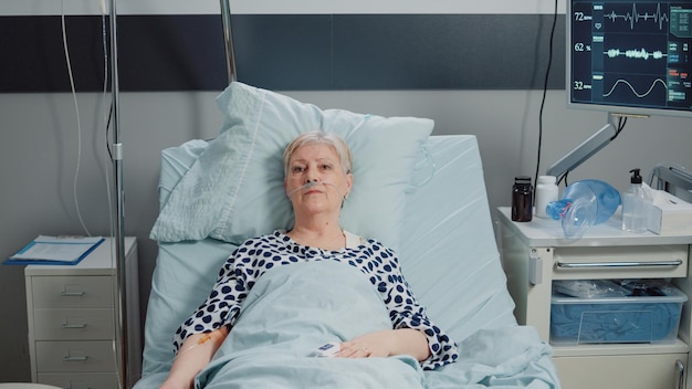 Patient âgé avec un sac d'égouttement IV et un tube nasal à oxygène allongé dans son lit. Femme âgée atteinte d'une maladie recevant des soins de santé pour se rétablir dans une salle d'hôpital, en attente d'un soutien médical.