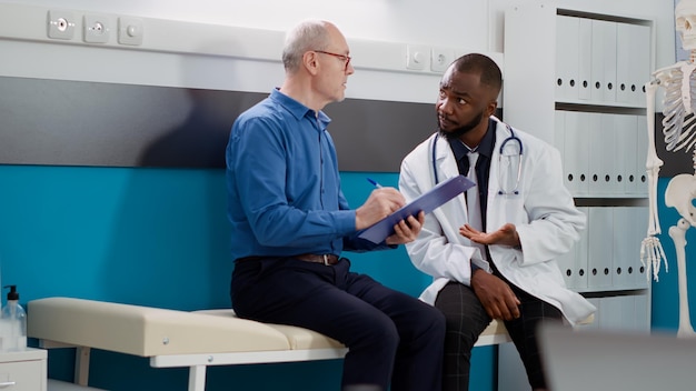 Patient âgé signant un formulaire de consultation pour recevoir des médicaments et un traitement sur ordonnance. Médecin aidant un vieil homme malade à guérir le diagnostic lors d'un rendez-vous d'examen.