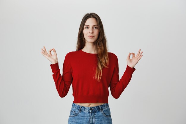 Patient et détendu, souriant jeune jolie femme méditant, tenir la main en geste mudra