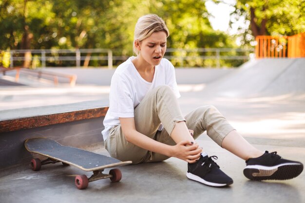 Une patineuse bouleversée tenant sa jambe douloureuse avec une planche à roulettes près tout en passant du temps au skatepark