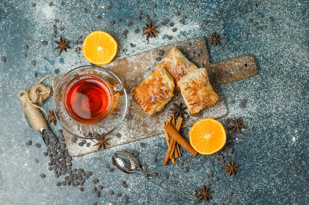 Pâtisseries avec farine, thé, orange, chips de choco, épices sur stuc et planche à découper, vue de dessus.