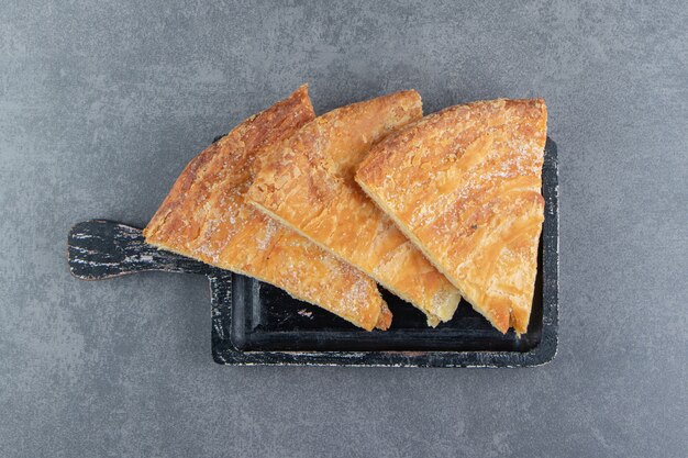 Pâtisseries en forme de triangle sur une planche à découper noire.