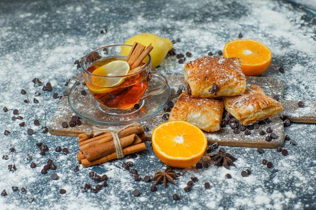 Pâtisseries avec thé, farine, chips de chocolat, épices, orange, citron high angle view sur béton et planche à découper