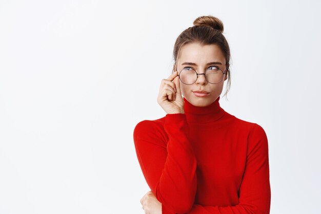 Patron de dame réfléchie dans des verres debout pensif regardant à gauche le logo ou le graphique et pensant debout dans les lunettes sur fond blanc