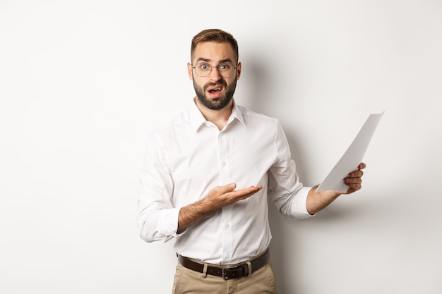 Patron déçu grondant pour un mauvais rapport, montrant des documents et ayant l'air confus, debout