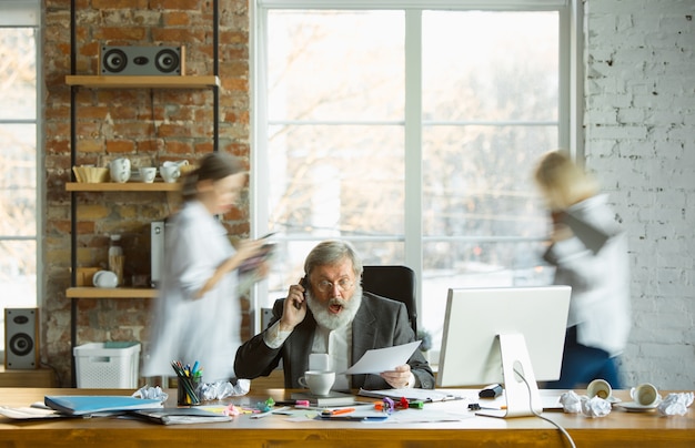 Patron nerveux et fatigué sur son lieu de travail occupé pendant que les gens se déplacent presque flous. Employé de bureau, gestionnaire de travail, a des problèmes et des délais, ses collègues distrayants. Entreprise, travail, concept de charge de travail.