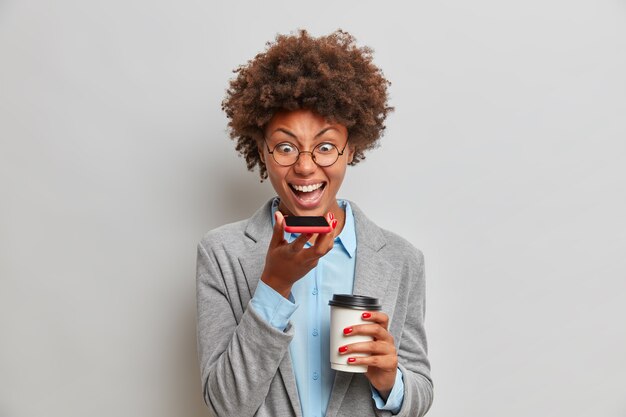 Patronne en colère en tenue formelle grise, a un appel vocal, crie avec colère sur un collègue qui a échoué dans le rapport d'activité, boit du café à emporter, passe du temps au bureau