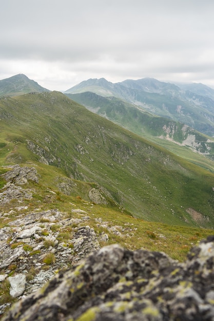 Paysage de collines couvertes de verdure avec des montagnes rocheuses sous un ciel nuageux