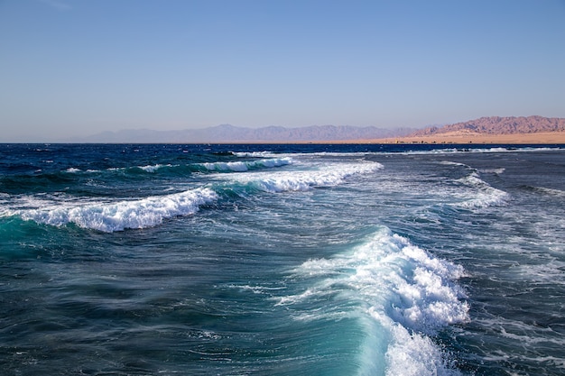 Paysage marin avec des vagues texturées et des silhouettes de montagne à l'horizon.