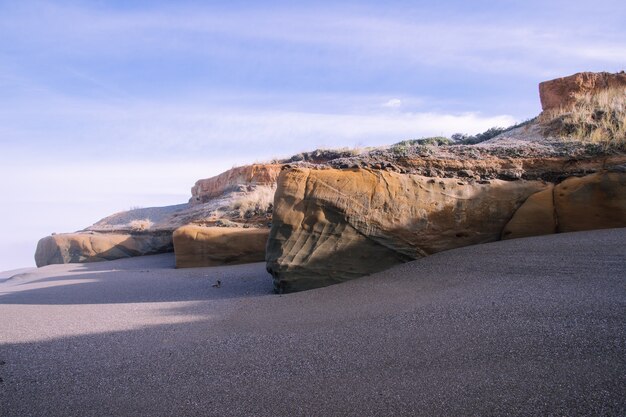 Paysage de la plage entouré de rochers sous la lumière du soleil et un ciel nuageux pendant la journée