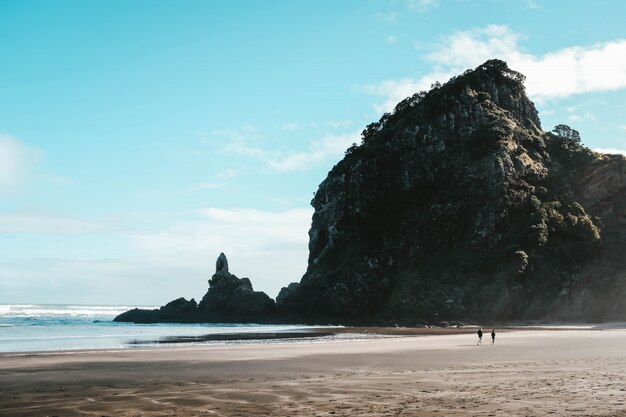 Paysage de la plage de Piha et de hauts rochers avec les gens qui se promènent sous un ciel bleu