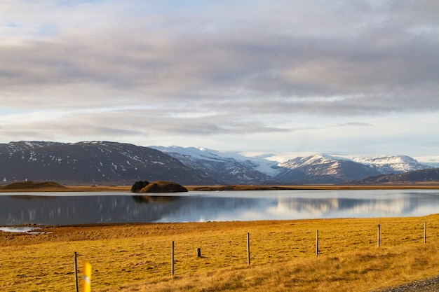 Paysage d'une rivière entourée de collines couvertes de neige et se reflétant sur l'eau en Islande