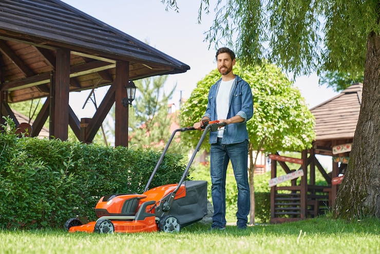 Photo gratuit un paysagiste souriant en chemise denim coupe la pelouse envahie avec un déménageur de pelouse en été.