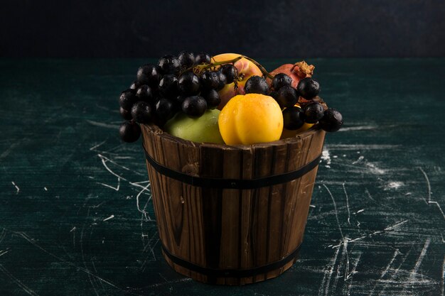 Pêches et raisins dans un seau en bois sur tableau noir