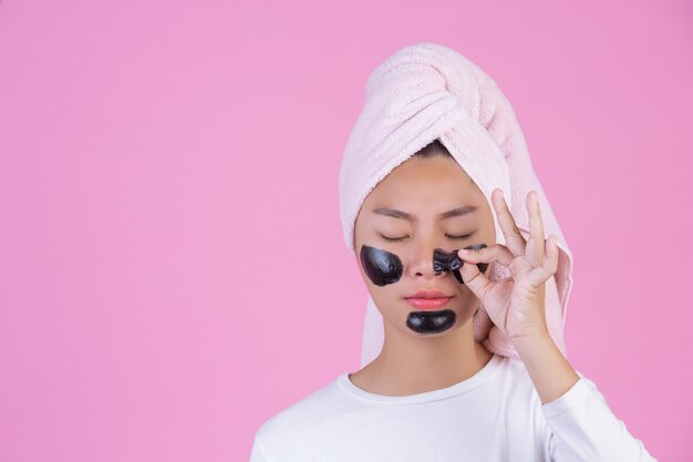 Peeling cosmétique beauté. Jeune femme avec un masque pelable noir sur la peau, produit de peeling cosmétique pour le soin de la peau sur le visage, de couleur rose.