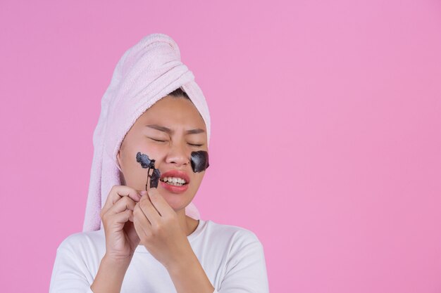 Peeling cosmétique beauté. Jeune femme avec un masque pelable noir sur la peau, produit de peeling cosmétique pour le soin de la peau sur le visage, de couleur rose.