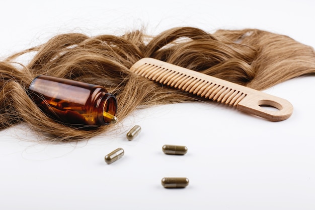 Peigne à cheveux en bois et une bouteille de vitamines se trouvent sur les boucles de cheveux bruns