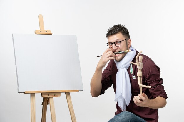 Peintre mâle vue de face essayant de dessiner sur un chevalet sur le mur blanc