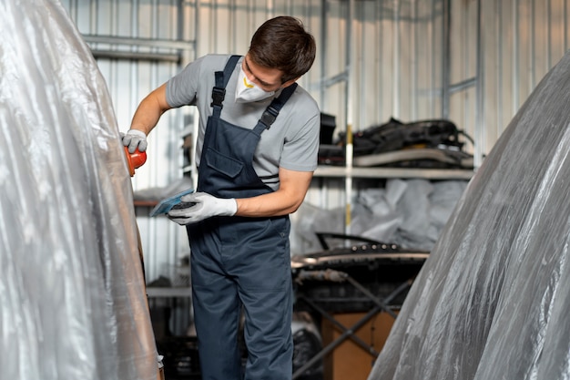 Photo gratuite peintre masculin en salopette faisant son travail à l'atelier de voiture